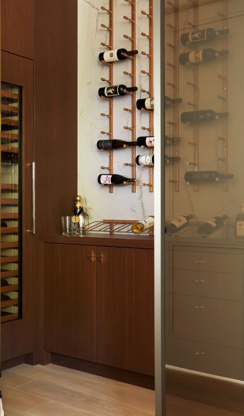 A wine room with a wine rack, storage and a built in fridge in the walnut cabinetry