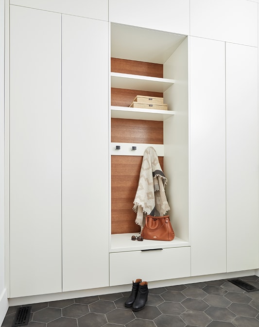 Flat white panel cabinetry surrounding brown wood stained custom cabinetry, with open shelves, bench seats, and drawer for storage. 