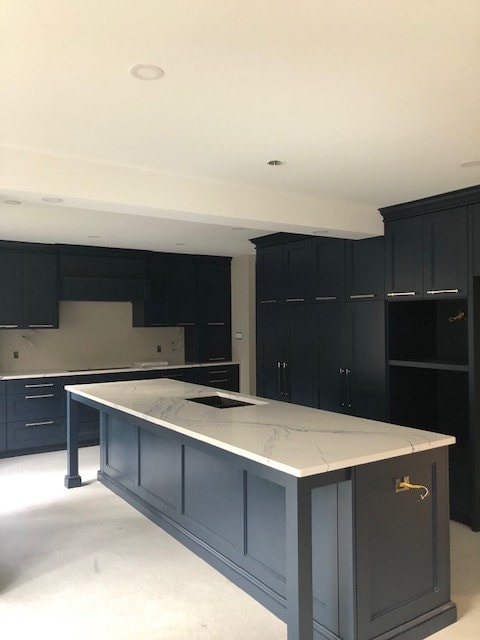 Step 3 of a kitchen install process. The kitchen is finalized with kitchen cabinets and countertop in place. Stunning dark blue-gray cabinetry with a marbled white countertop.