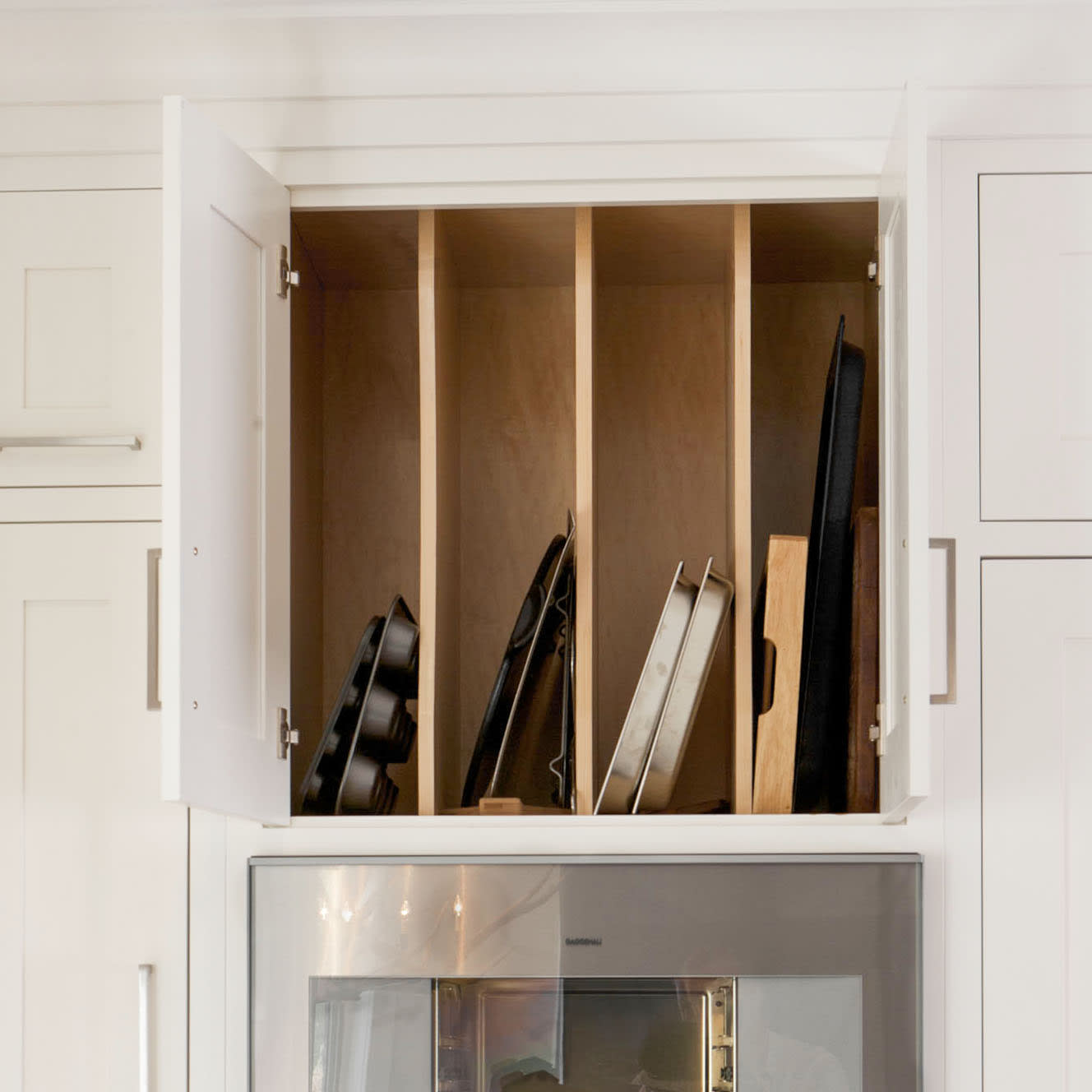 White kitchen cabinets with an over the stove storage cabinet with horizontal dividers for baking pans
