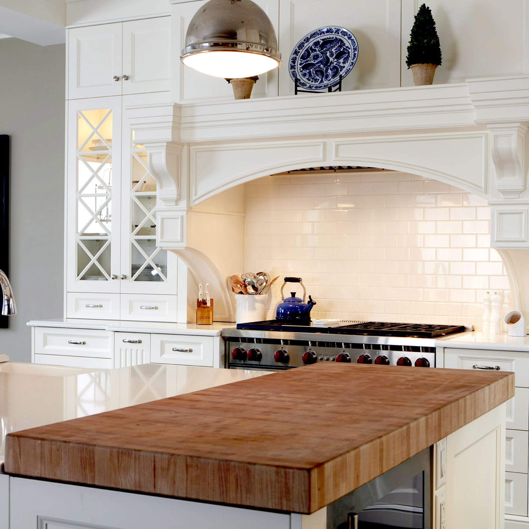 White kitchen with a butcher block and stone countertop and detailed cabinetry and built-in range hood
