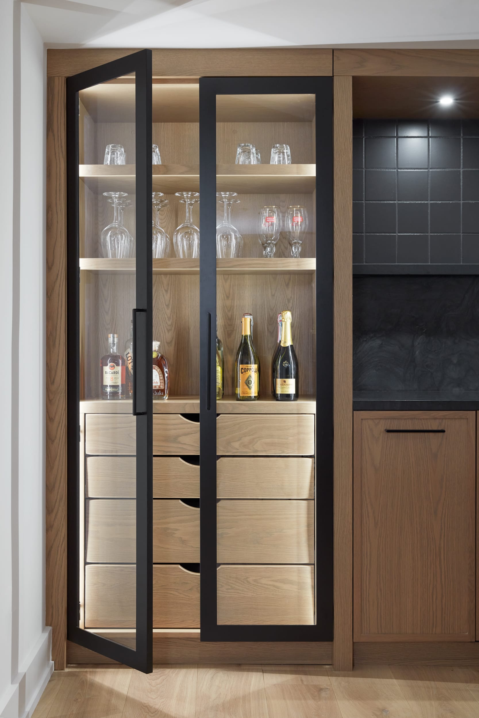 A transitional white oak basement bar with black and glass doors