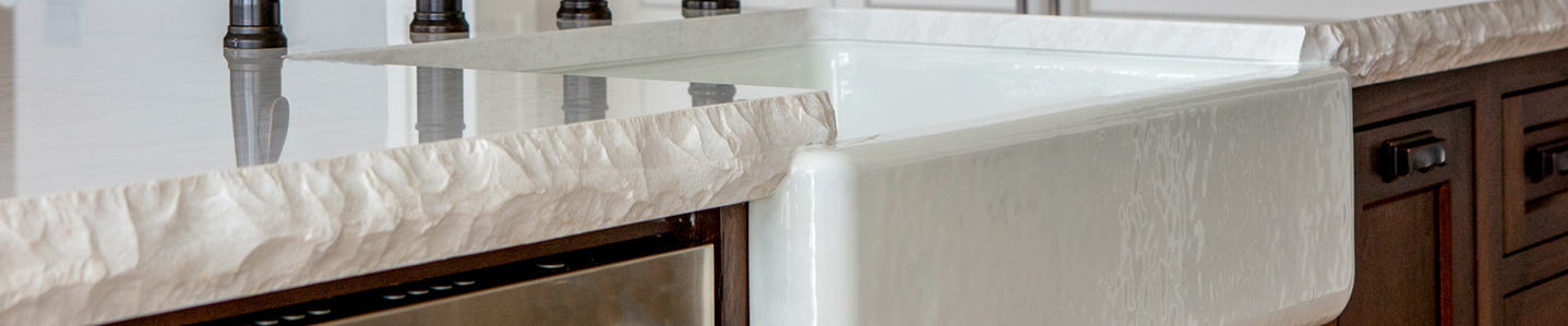 White stone kitchen countertop with chiseled countertop edge profile and white apron front sink and dark wood cabinets