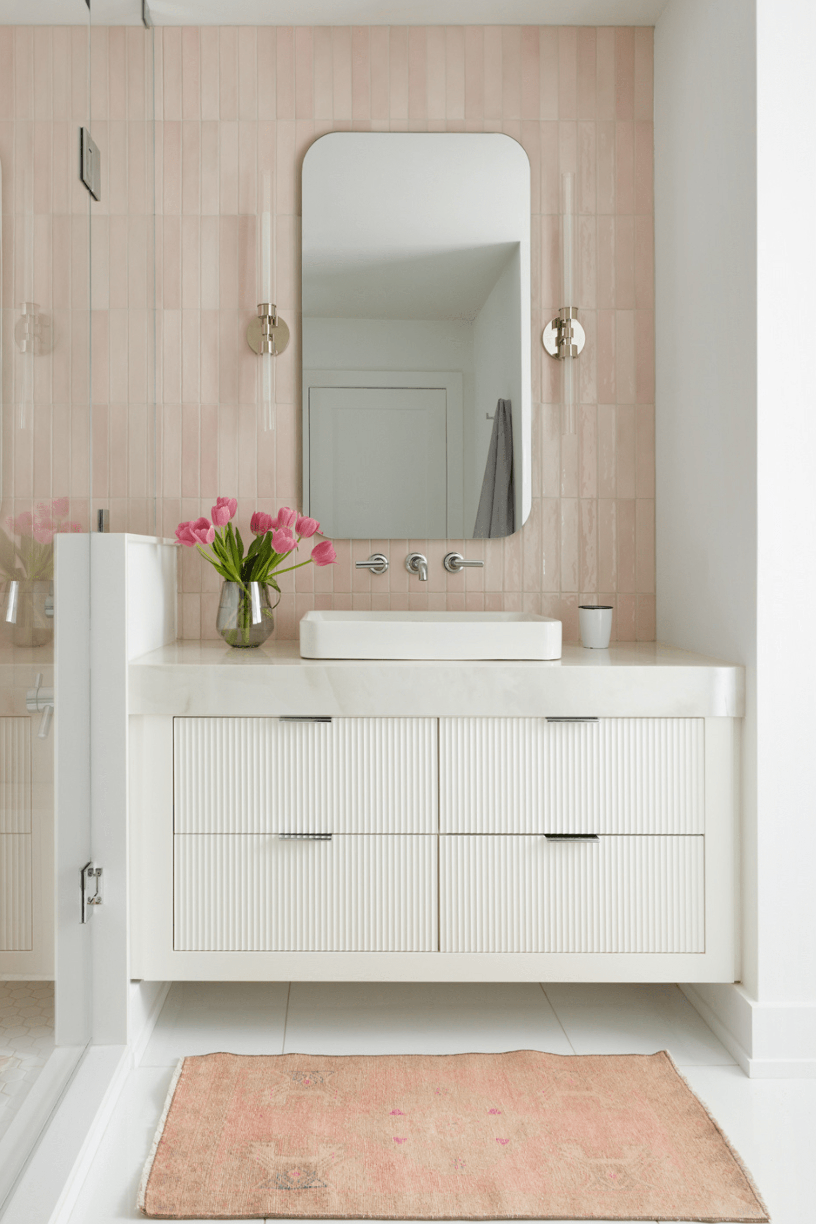 A floating white fluted vanity with pink wall tiles