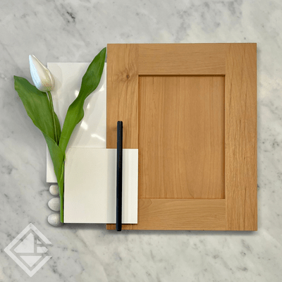 Alder wood cabinet door with black pull alongside a painted white MDF sample with white quartz and natural elements