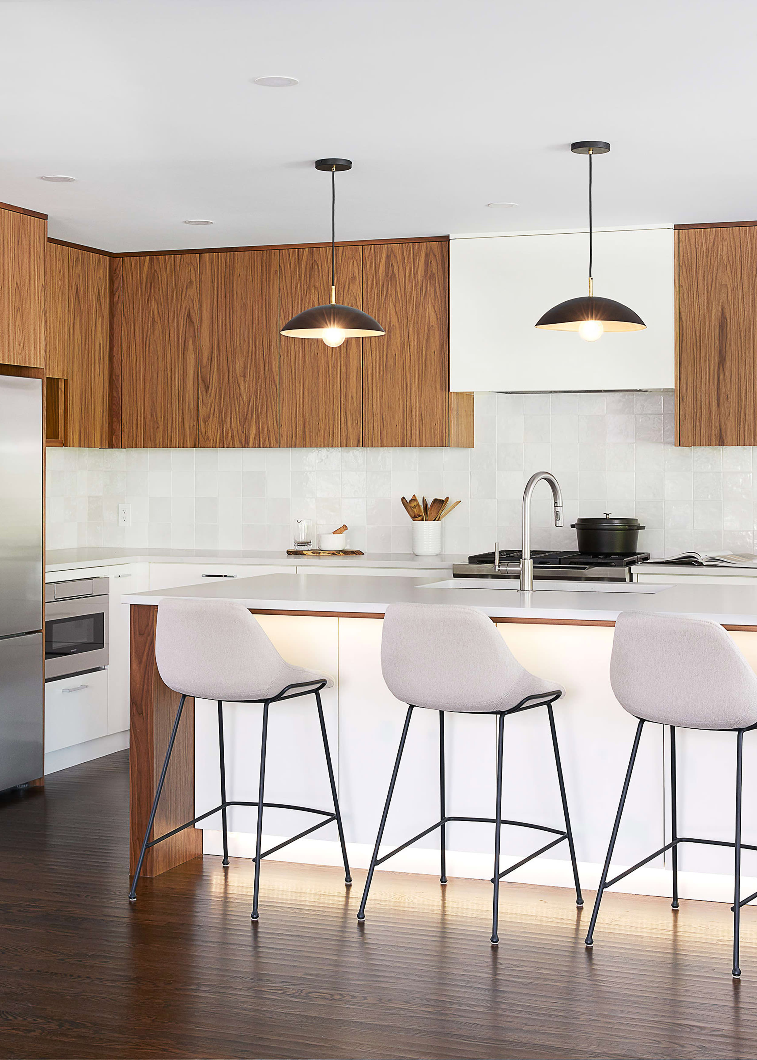 Modern kitchen with walnut uppers, white lower cabinets, and plush cream stools at the island
