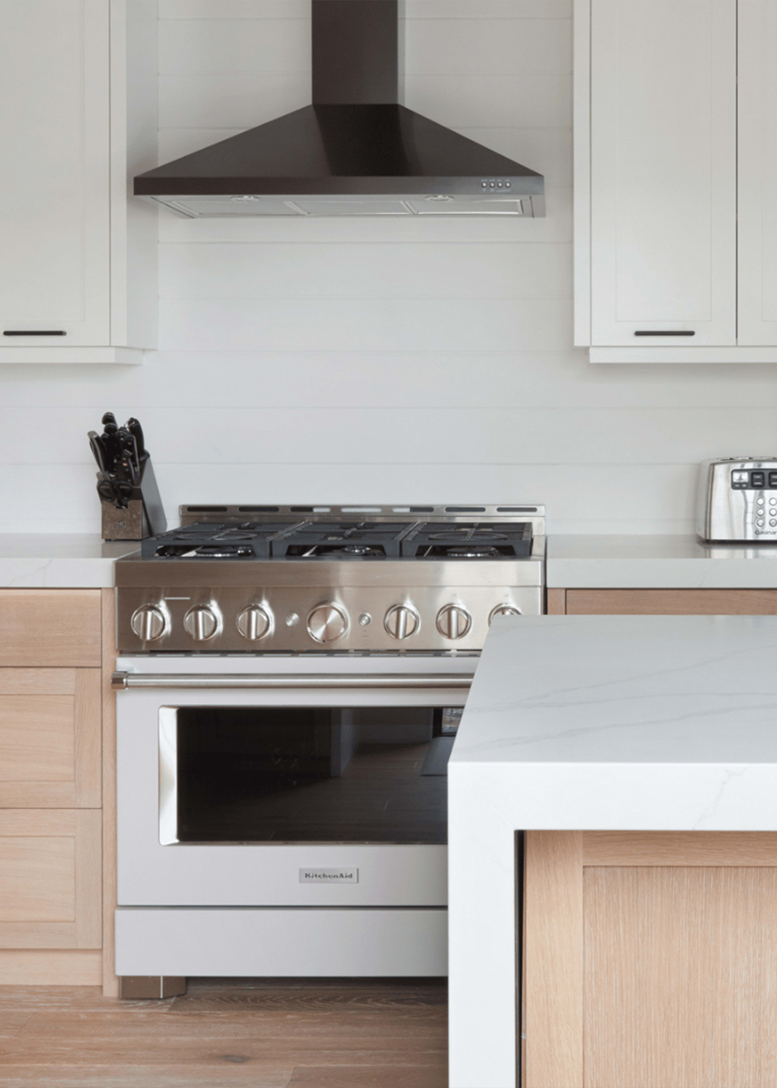 Bright kitchen with white upper cabinetry and white oak lower cabinets and a stainless steel gas stove and range hood