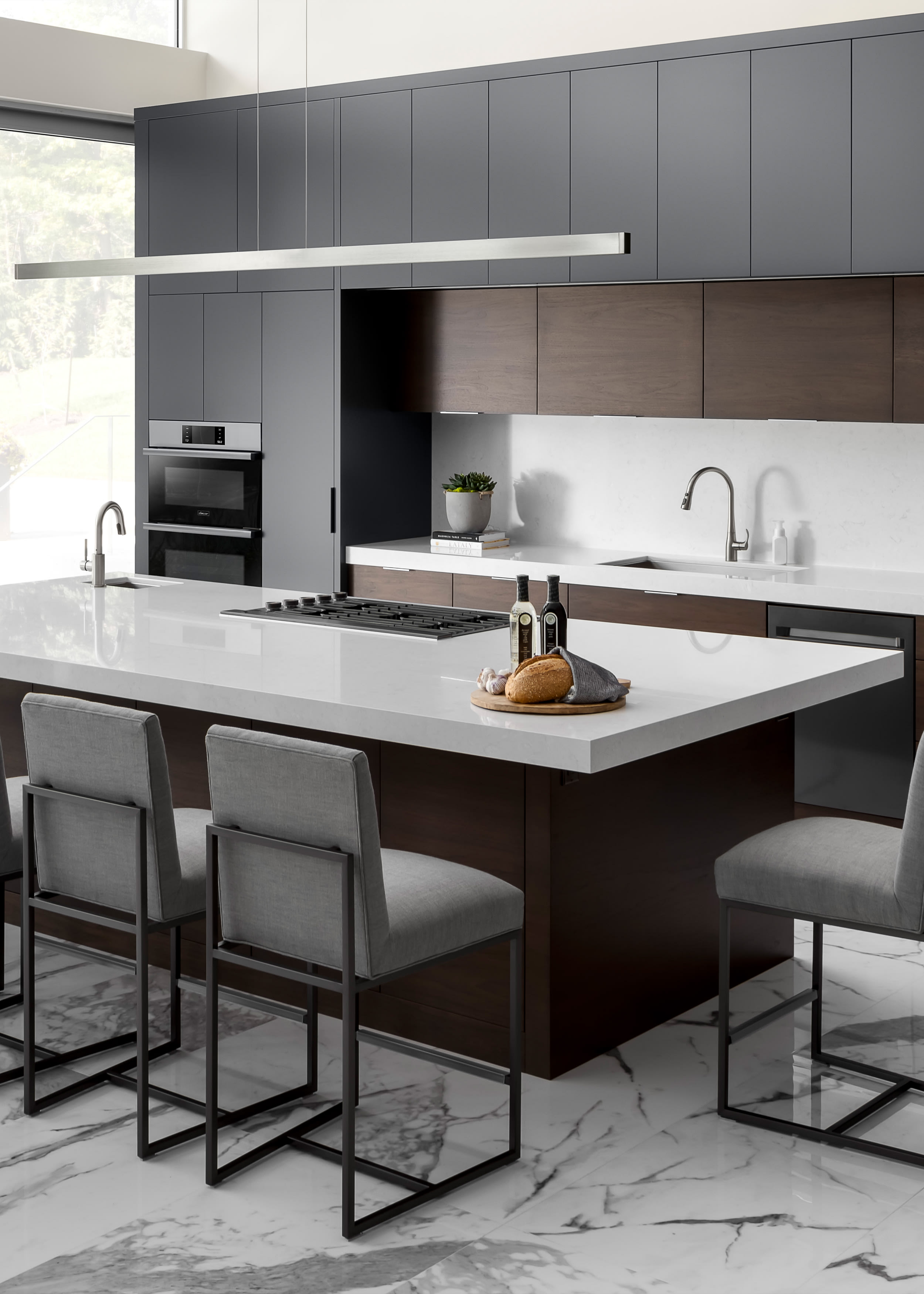 Moody, minimal kitchen with dark gray and walnut slab cabinets. Gray upholstered stools arranged around the island