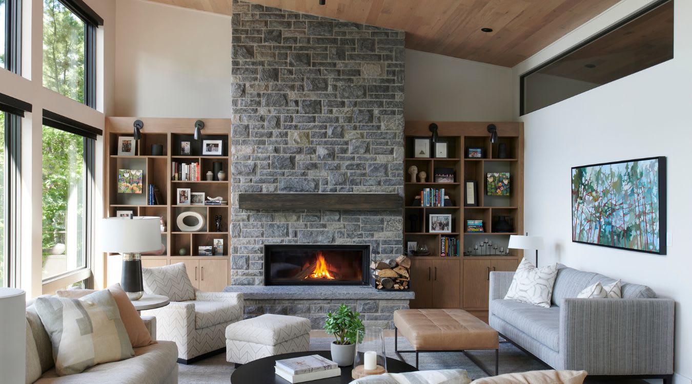 A modern, airy living room with a tall gray, stone mantel and white oak built-in shelves on either side