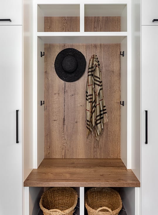 Brown wood stained custom cabinetry with hooks to hang items, bench seat, and open shelves. 