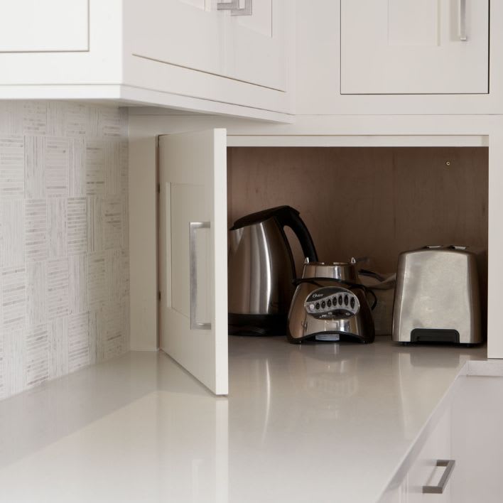 Appliance garage with door open in corner kitchen cabinet displaying toaster and kettle.