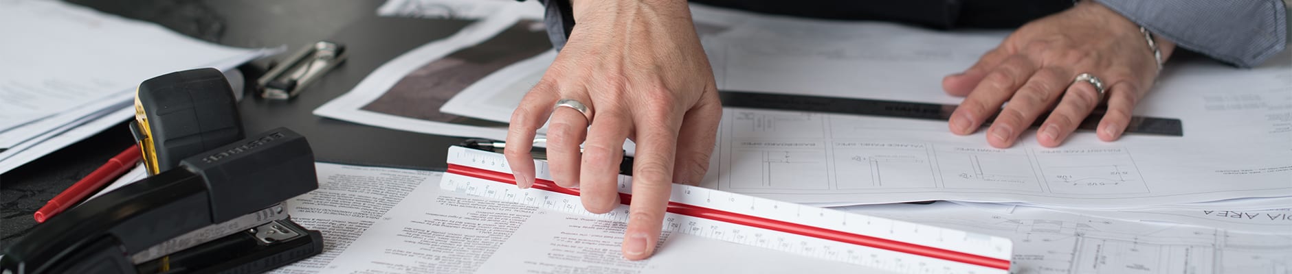Close up of two hands holding ruler and pointing to blueprint of designs