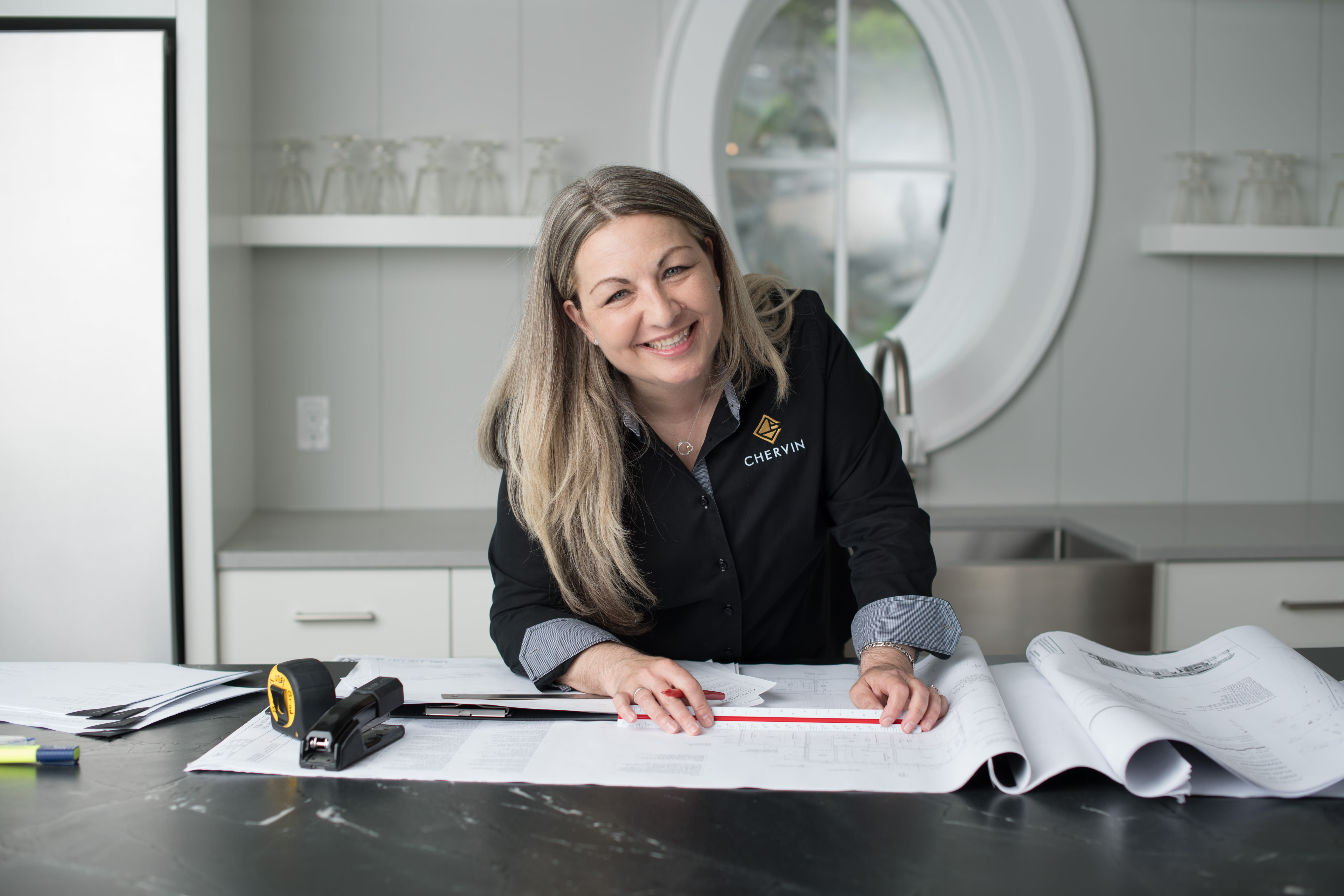 Photo of Chervin designer, Lisa, smiling at the camera with blueprints and tools spread out on a counter