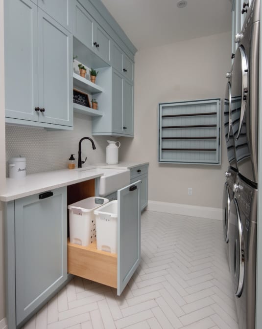 Custom blue cabinetry in a laundry room with a drying rack and pull out laundry hampers